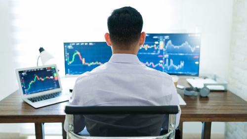 Back of a business man sitting at his desk looking at graphs on his computer