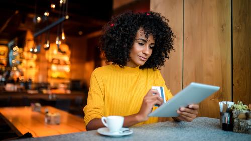 Commercial Card Solutions Young woman using her credit card and ipad in a coffee shop