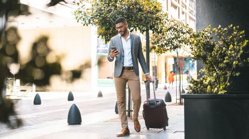 Commercial Checking Accounts person looking at phone walking down the sidewalk with luggage