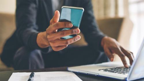Fraud Protection Closeup of hand holding cellphone and other hand typing on laptop