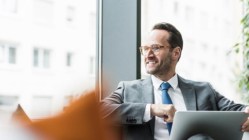 Business Man sitting on couch with laptop looking outside window