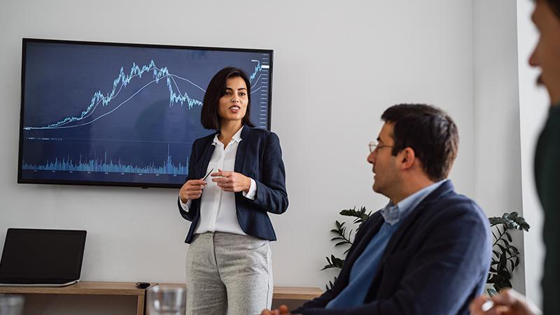 Business woman presenting with a stock chart in the background to colleagues