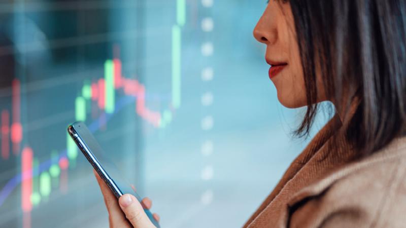 Investment Insights Business woman looking at phone in front of stock chart