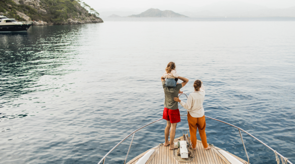 View from behind of happy family travelling with baby on board of luxury yacht