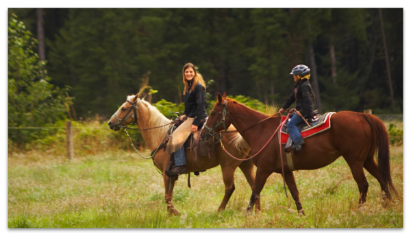 Woman and girl riding horses in field.