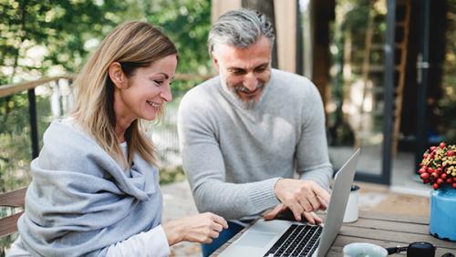 Photo of a happy couple doing finances in backyard.