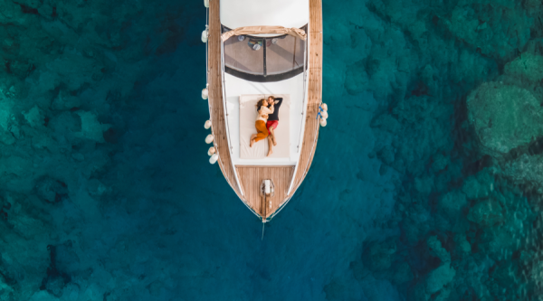 Aerial drone view of couple in love on board of luxury yacht anchored in tropical paradise bay with emerald clear water